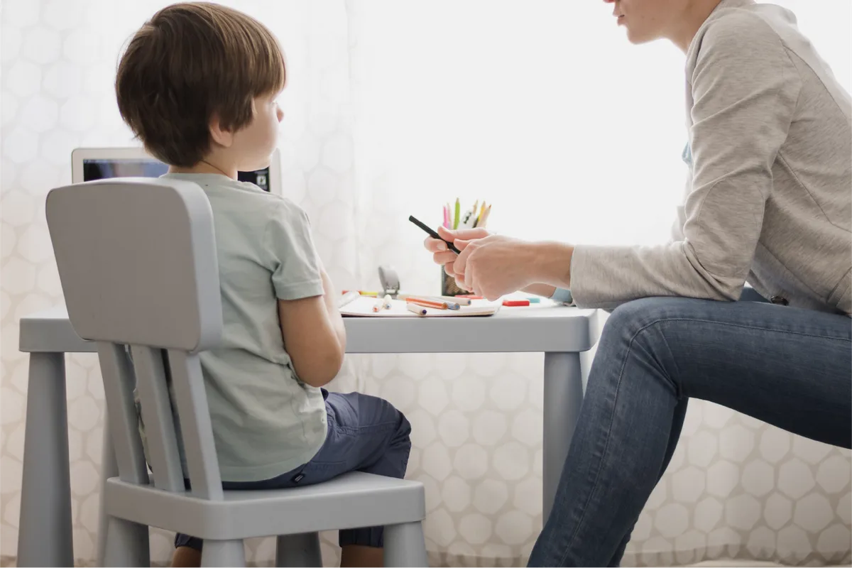 A practitioner sitting beside a young child at a desk, guiding a drawing activity